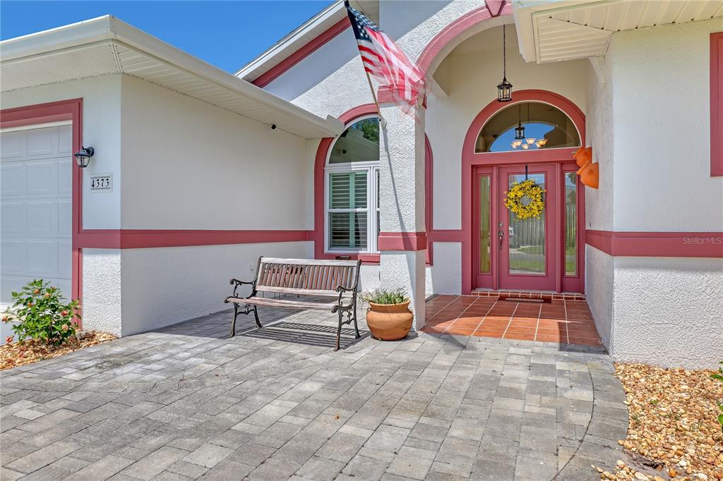 A paved patio leads to the front entrance of a house with white stucco walls — 4373 FLETCHER LANE, TITUSVILLE, FL