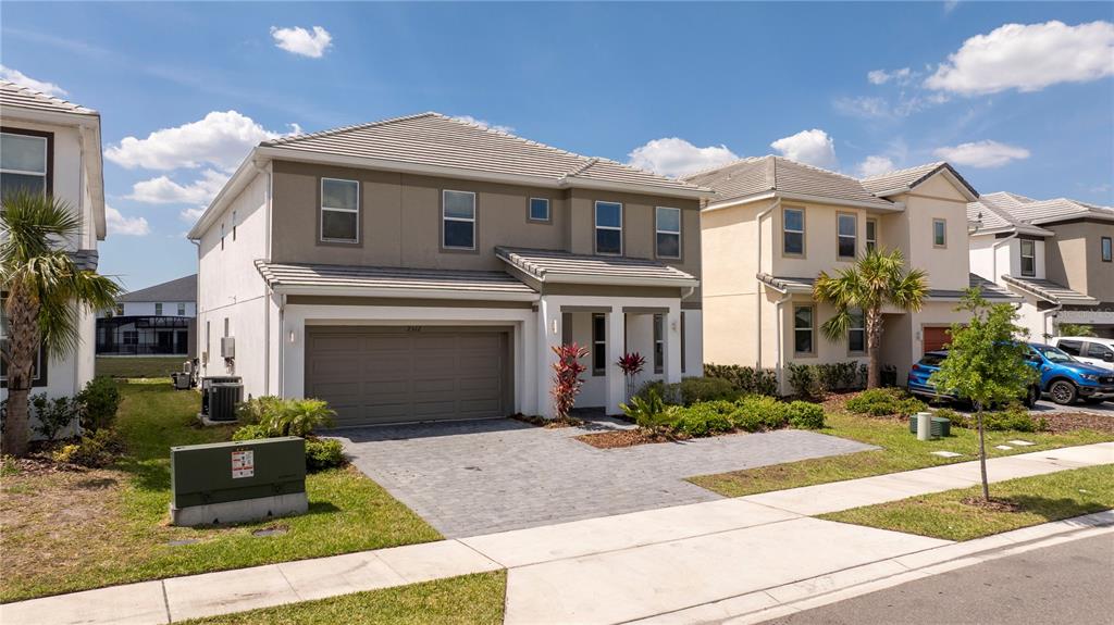 A two-story suburban house with a gray garage, tan stucco siding, and a paved driveway — 2512 SHANTI DRIVE, KISSIMMEE, FL
