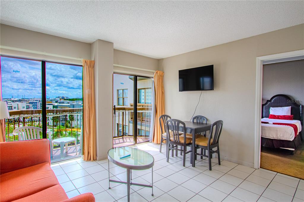 A living and dining area with tile floors, a balcony, and an adjacent bedroom — 6165 CARRIER DRIVE UNIT 2804, ORLANDO, FL