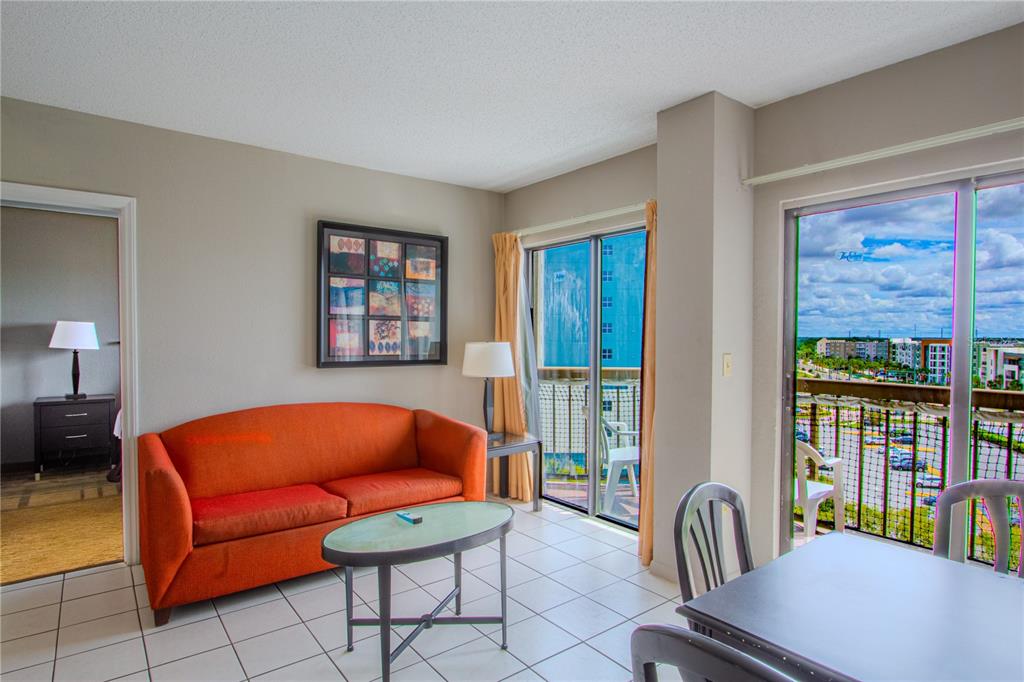 A living room with an orange sofa, glass coffee table, and a balcony with outdoor views — 6165 CARRIER DRIVE UNIT 2804, ORLANDO, FL