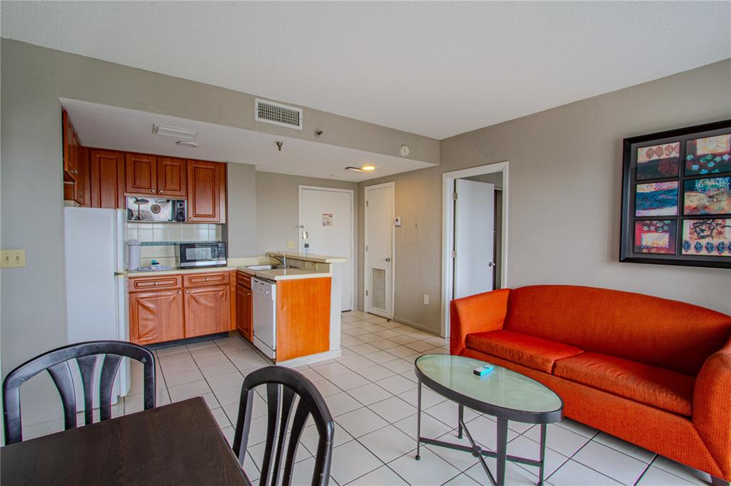 A small kitchen with wood cabinets and a living area with an orange sofa — 6165 CARRIER DRIVE UNIT 2804, ORLANDO, FL