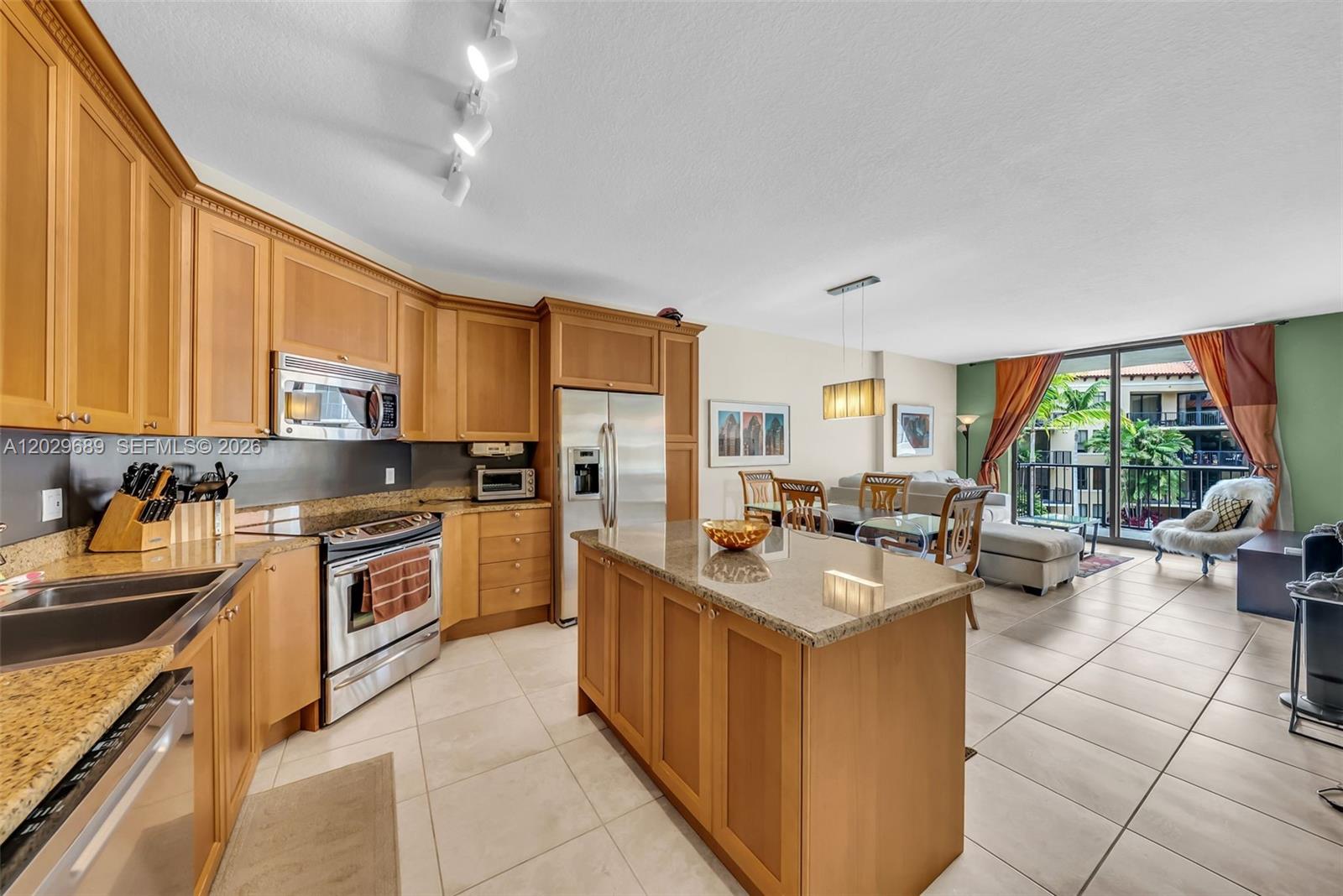 A kitchen with wood cabinets and granite countertops opens into a dining and living area — 55 Merrick Way # 709, Coral Gables FL 33134, CORAL GABLES, FL