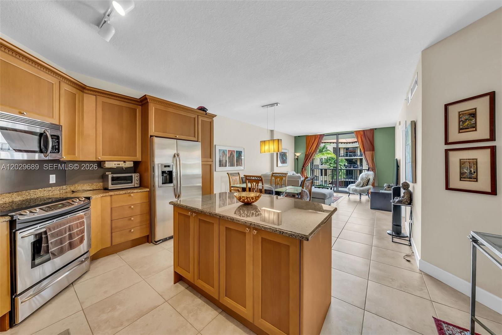 A kitchen with wood cabinets and a granite island opens to a living area — 55 Merrick Way # 709, Coral Gables FL 33134, CORAL GABLES, FL