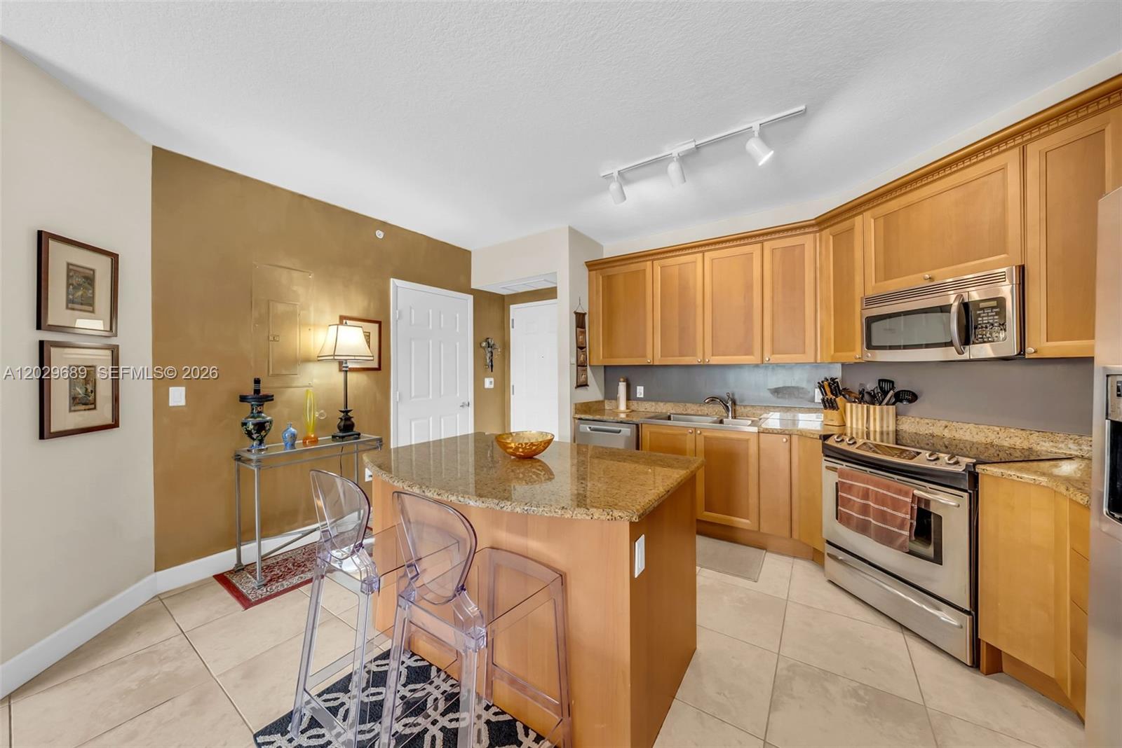 A kitchen features light wood cabinets, granite countertops, a central island, and stainless steel appliances — 55 Merrick Way # 709, Coral Gables FL 33134, CORAL GABLES, FL