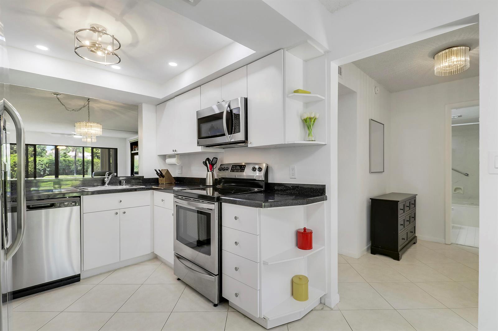 A white kitchen features stainless steel appliances, black countertops, and tile flooring — 5121 Oak Hill Lane # 412, Delray Beach FL 33484, DELRAY BEACH, FL