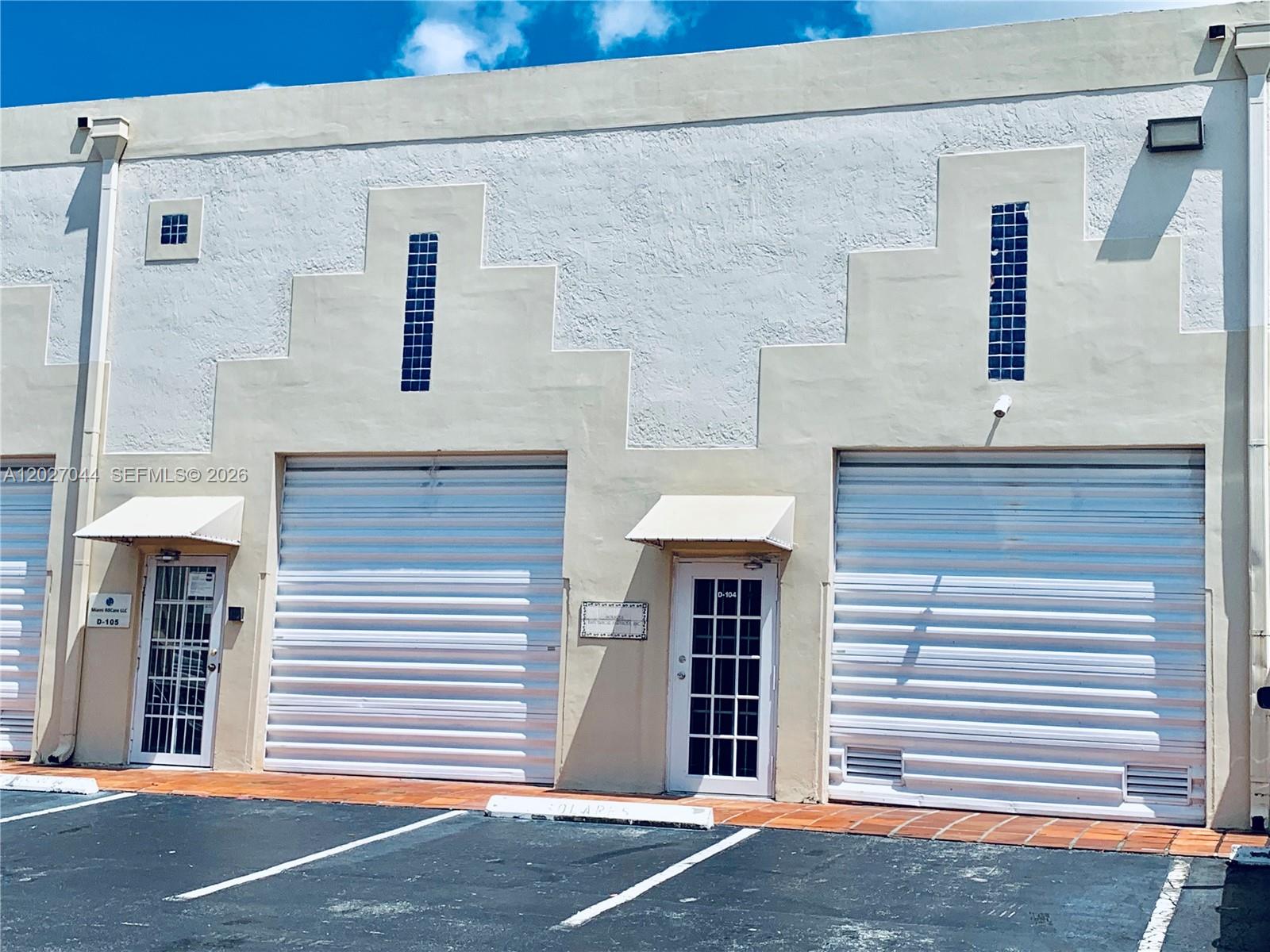 The exterior of a commercial building features two roll-up garage doors and two glass-paneled doors — 10421 NW 28 ST # 104, FL 33172, FL