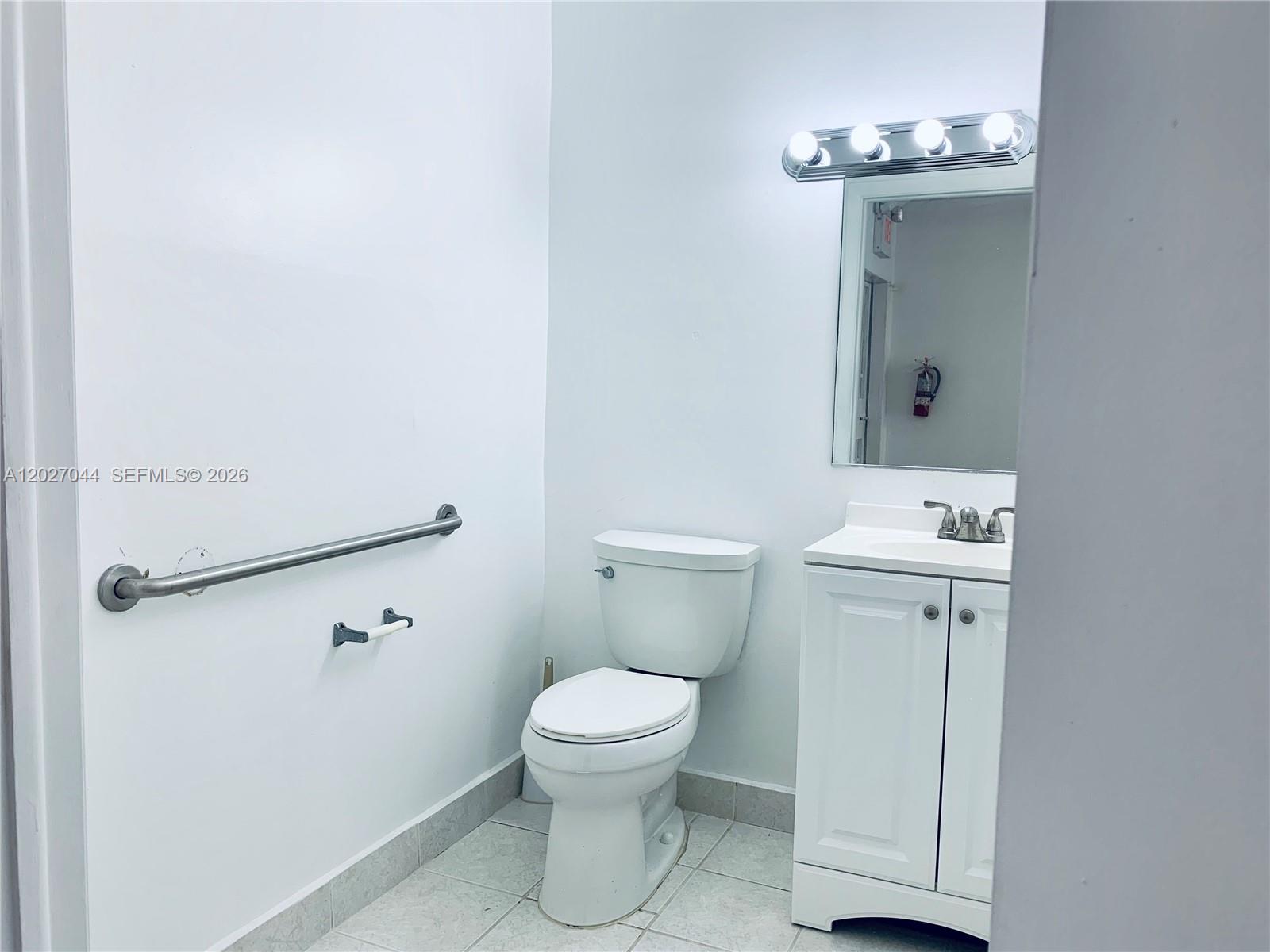 A small bathroom features a white toilet, a vanity with a mirror, and a grab bar — 10421 NW 28 ST # 104, FL 33172, FL