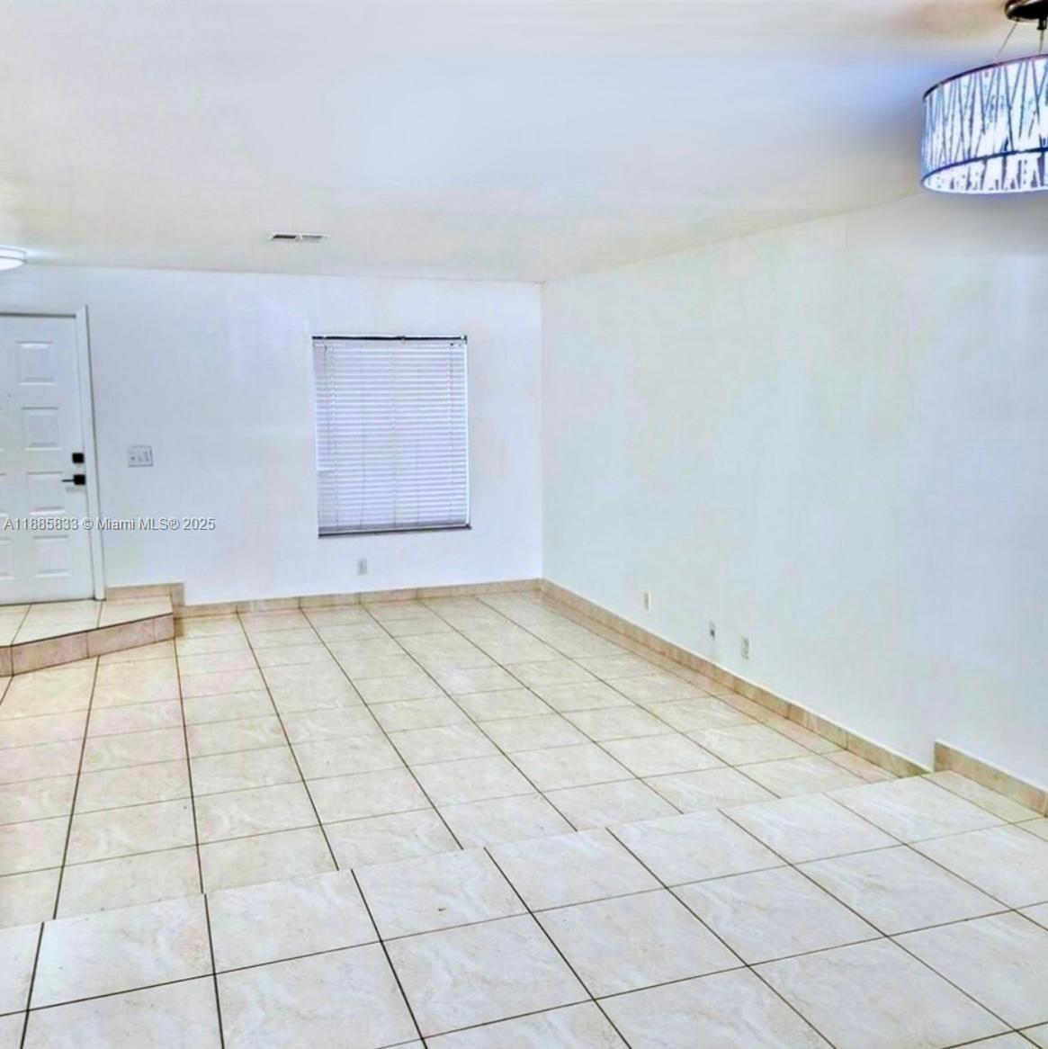 An empty room features white walls, light-colored tile flooring, a window with blinds, and a chandelier — 5164 S University Dr, Davie FL 33328, DAVIE, FL