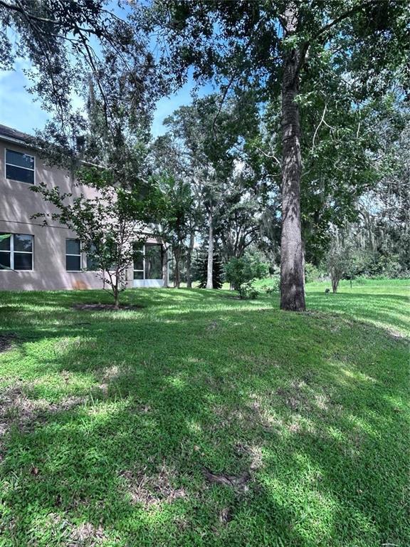 A two-story house with a screened-in porch sits beside a grassy yard and large trees — 1531 MCCREA DRIVE, LUTZ, FL