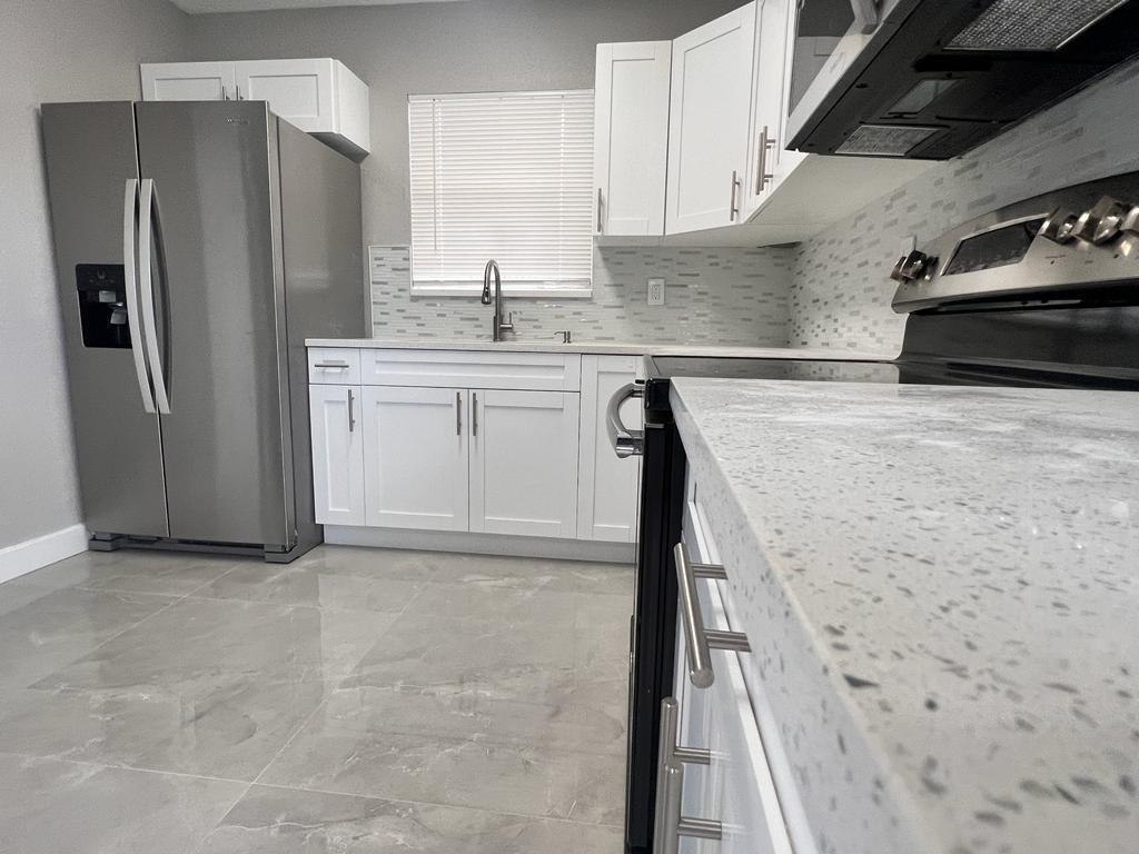 A kitchen features white cabinets, stainless steel appliances, a tiled backsplash, and light-colored countertops — 151 NE 17th Avenue, Boynton Beach FL 33435, BOYNTON BEACH, FL