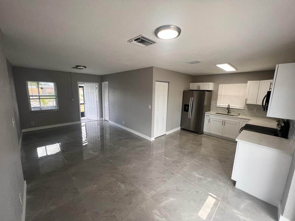 An open-concept kitchen and living area features gray tile flooring, white cabinets, and stainless appliances — 151 NE 17th Avenue, Boynton Beach FL 33435, BOYNTON BEACH, FL