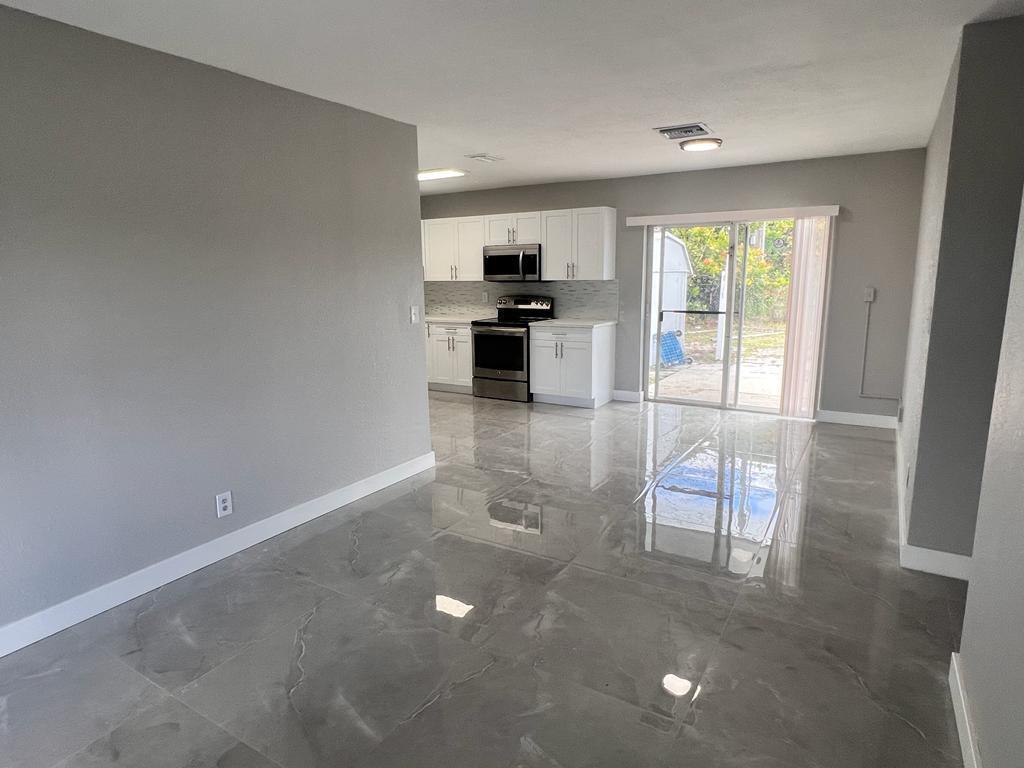 A kitchen with white cabinets and stainless steel appliances opens to a gray-tiled living area — 151 NE 17th Avenue, Boynton Beach FL 33435, BOYNTON BEACH, FL