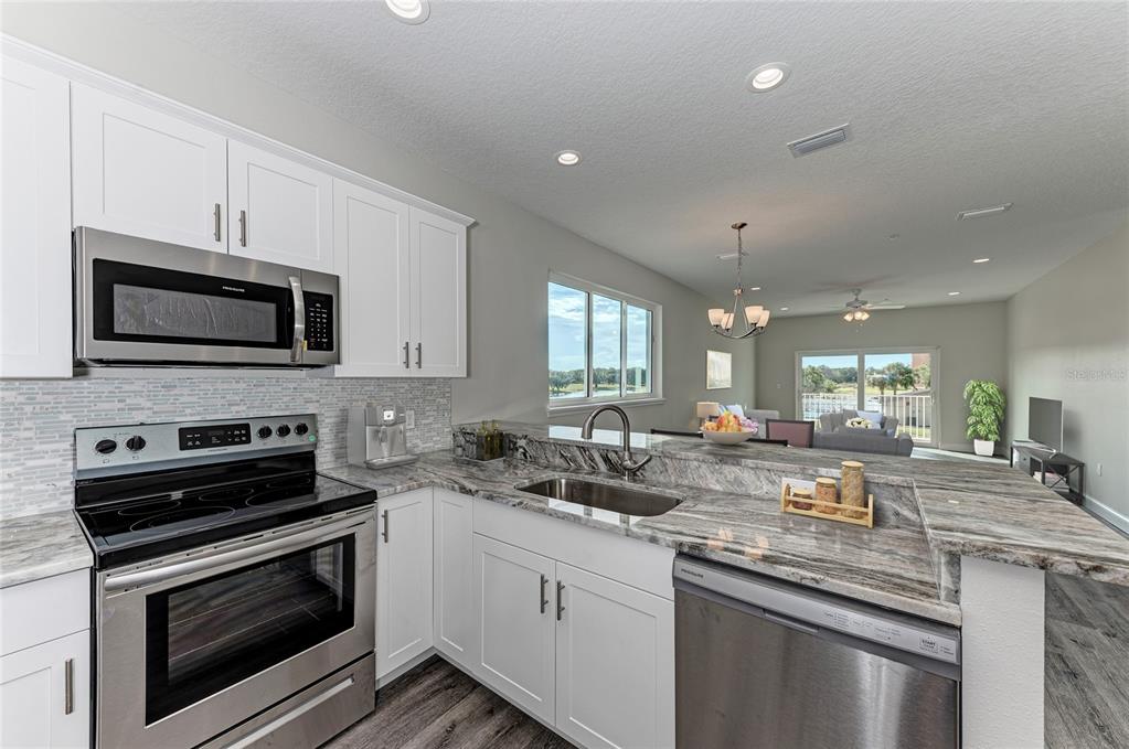 A kitchen with white cabinets, stainless steel appliances, and granite countertops overlooks a living area — 2225 14TH AVENUE W UNIT 201, PALMETTO, FL