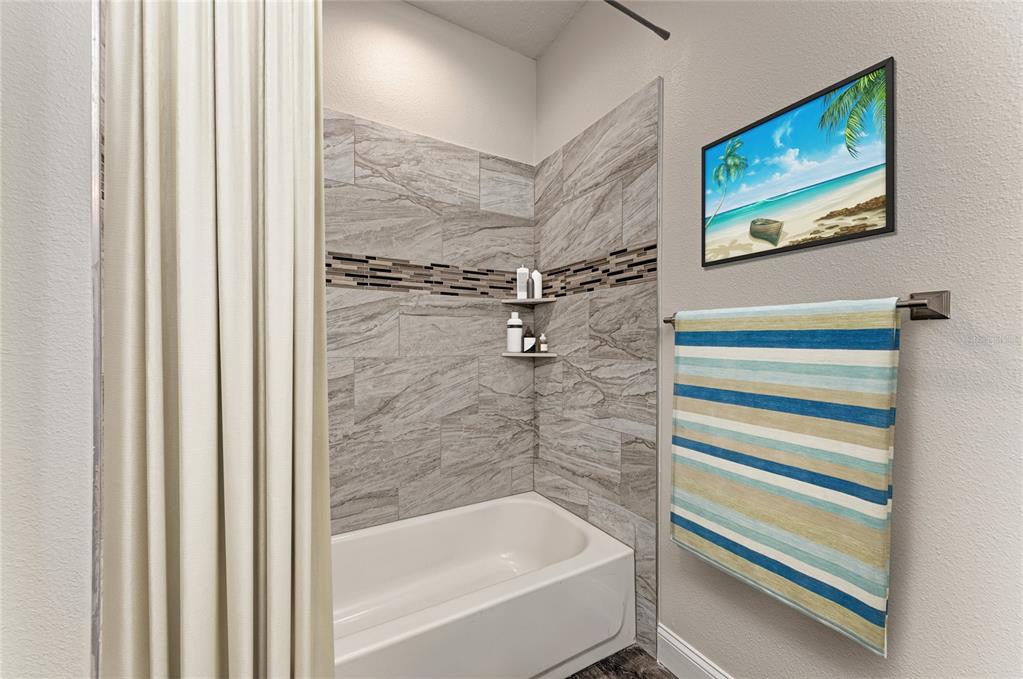A bathroom features a white bathtub, gray tiled walls with a decorative accent strip, and a towel — 2225 14TH AVENUE W UNIT 201, PALMETTO, FL