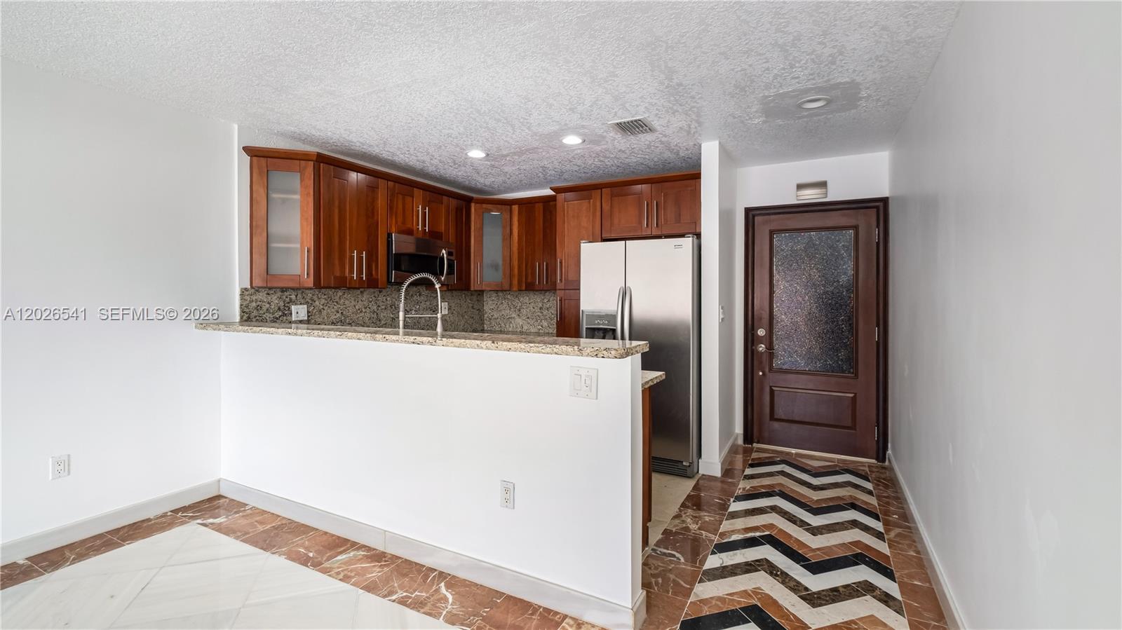 A kitchen features wood cabinets, granite countertops, stainless steel appliances, and a chevron-patterned floor — 4390 W 12th Ln # 18B, Hialeah FL 33012, HIALEAH, FL