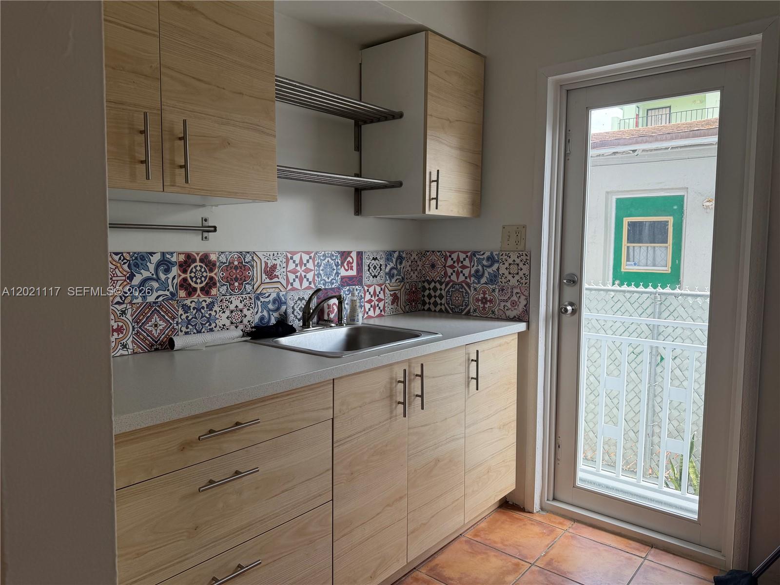 A kitchen features light wood cabinets, a patterned tile backsplash, and a glass-paned exterior door — 500 77th St # 2, Miami Beach FL 33141, MIAMI BEACH, FL