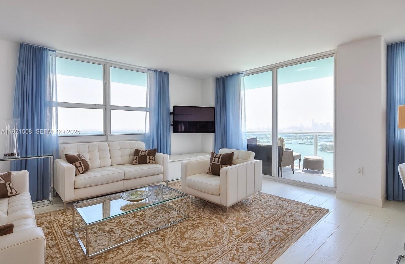 A bright living room features white leather furniture, a glass coffee table, and floor-to-ceiling windows — 650 West Ave # 2801, Miami Beach FL 33139, MIAMI BEACH, FL