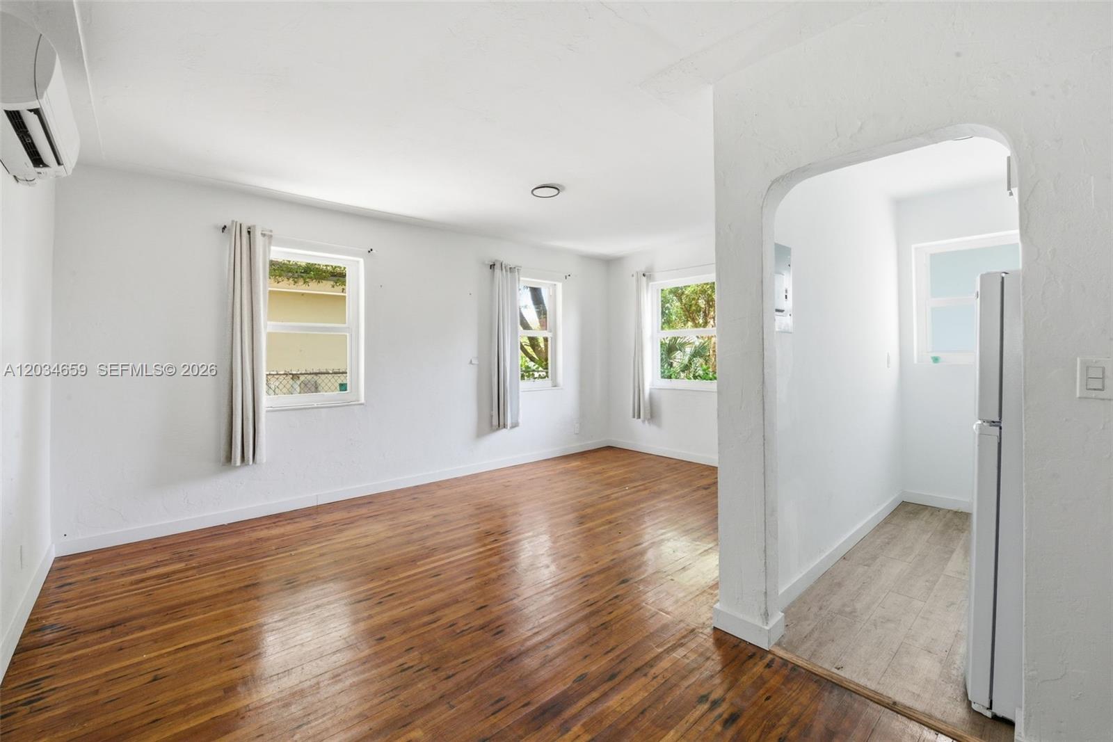 A living room with hardwood floors and white walls leads into a kitchen area — 101 NW 74th St # 4, Miami FL 33150, MIAMI, FL