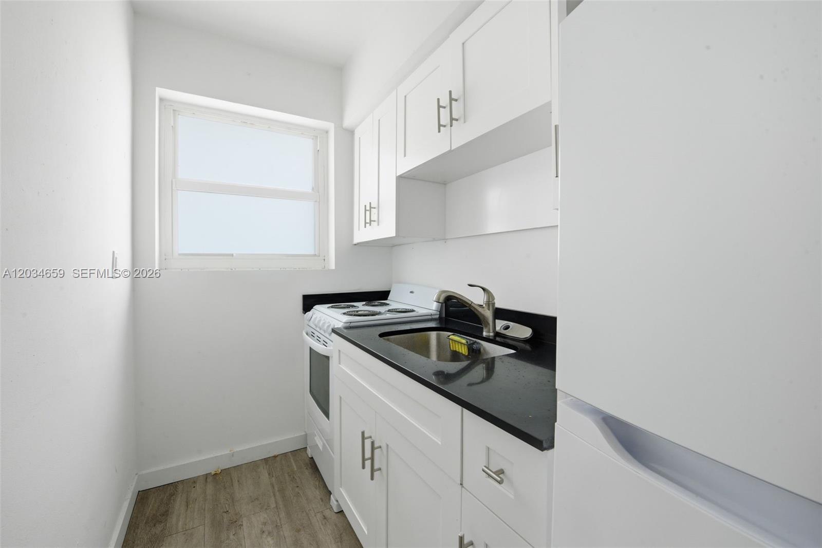 A small kitchen features white cabinets, a black countertop, a sink, and a stove — 101 NW 74th St # 4, Miami FL 33150, MIAMI, FL