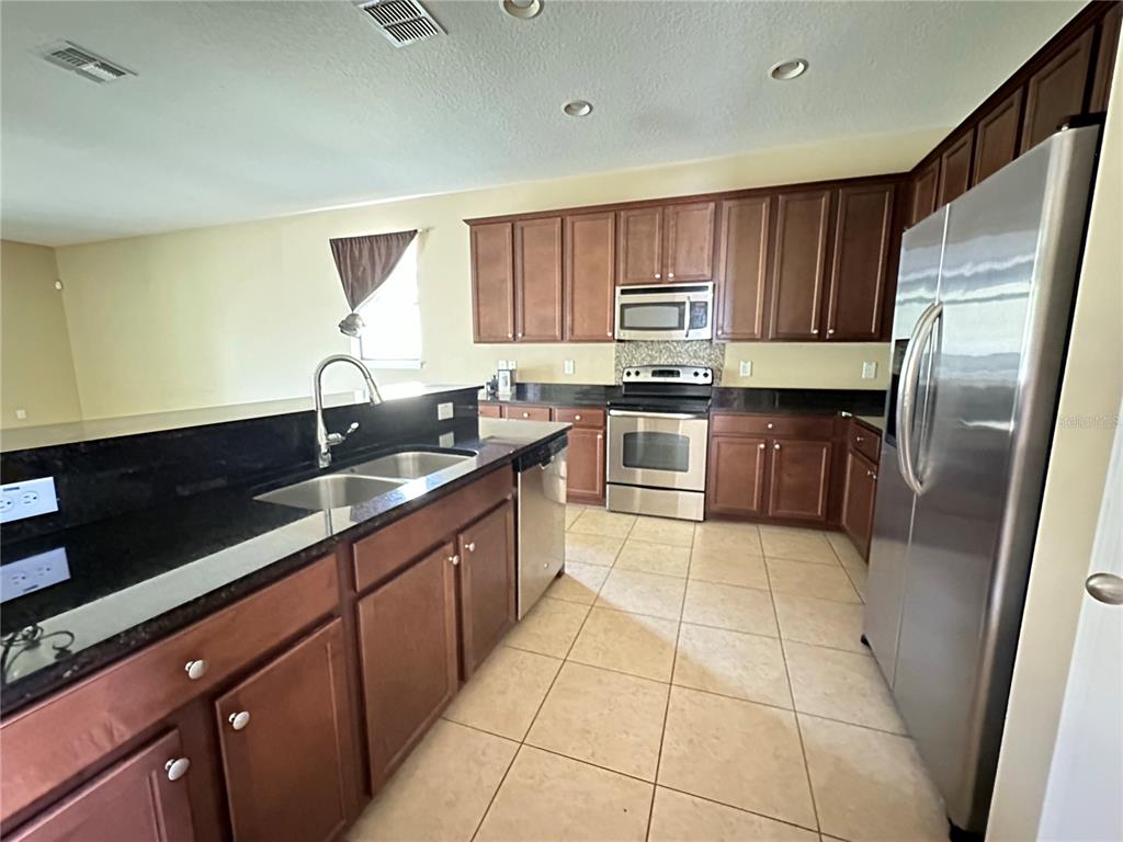 A kitchen features dark wood cabinets, black granite countertops, and stainless steel appliances — 13330 LONGACRE DRIVE, WINDERMERE, FL