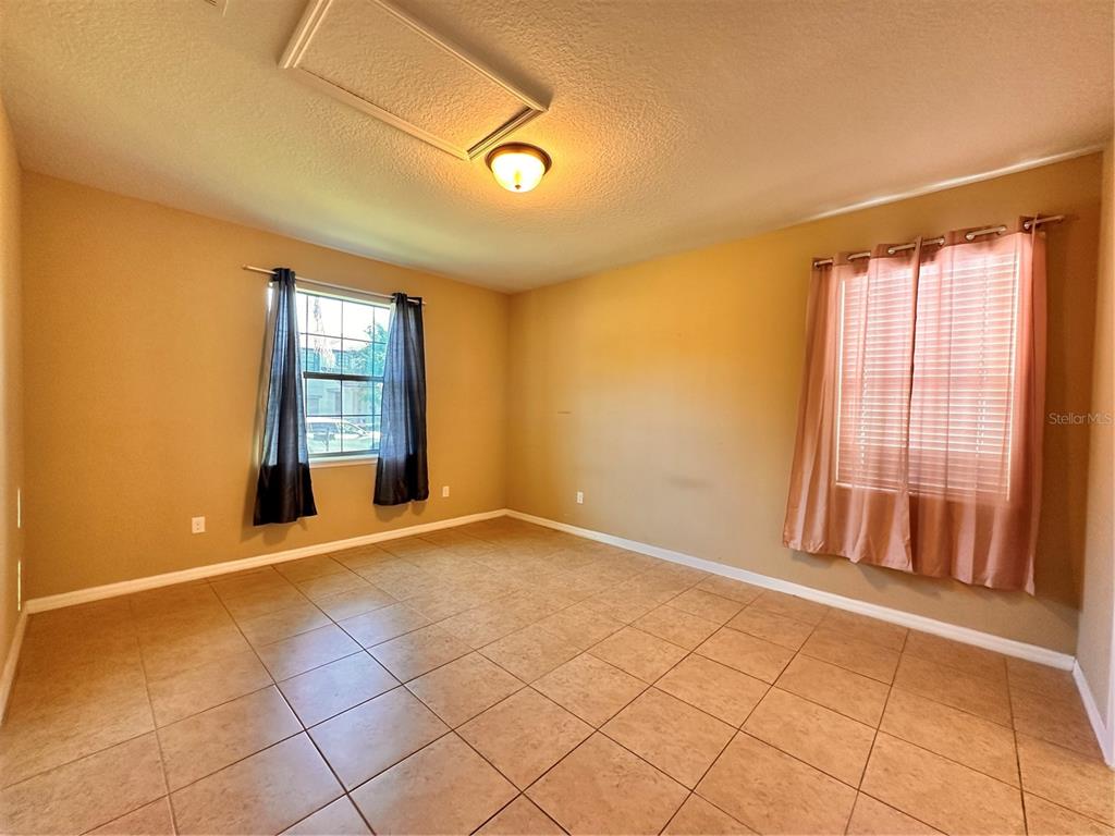 An empty room features tan walls, tiled flooring, two windows with curtains, and a ceiling light — 13330 LONGACRE DRIVE, WINDERMERE, FL