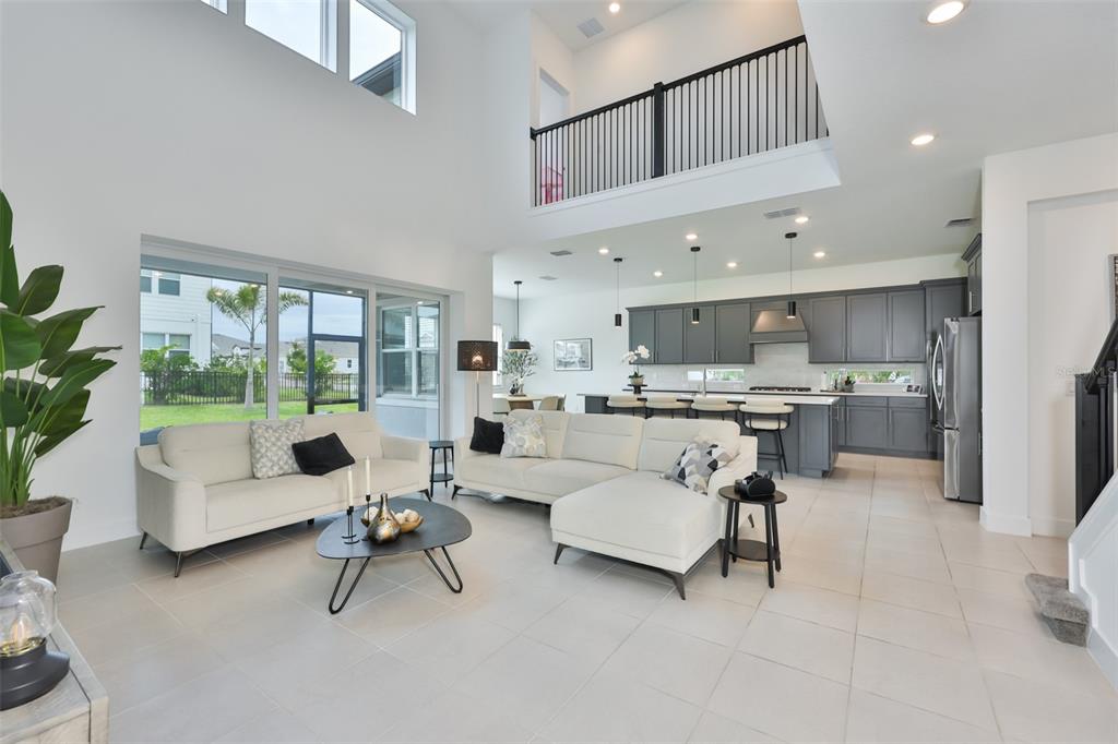 A bright, open-concept living room and kitchen featuring white tile floors and a lofted balcony — 6107 GOLDEN BEACH DRIVE, APOLLO BEACH, FL