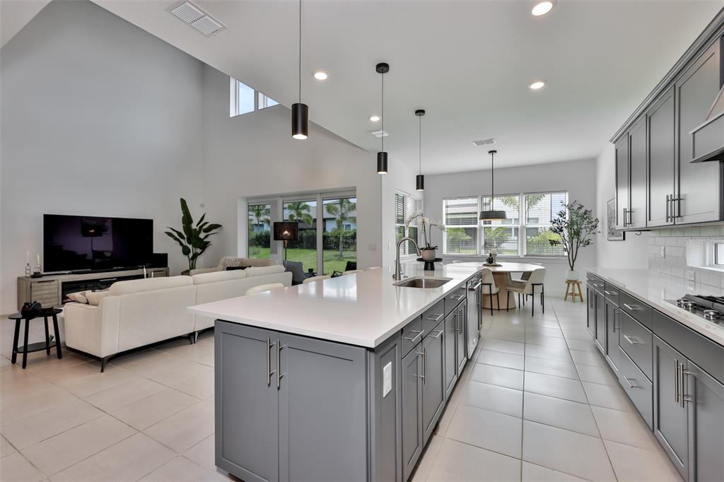 An open-concept kitchen with gray cabinets and a large island overlooks a living area — 6107 GOLDEN BEACH DRIVE, APOLLO BEACH, FL