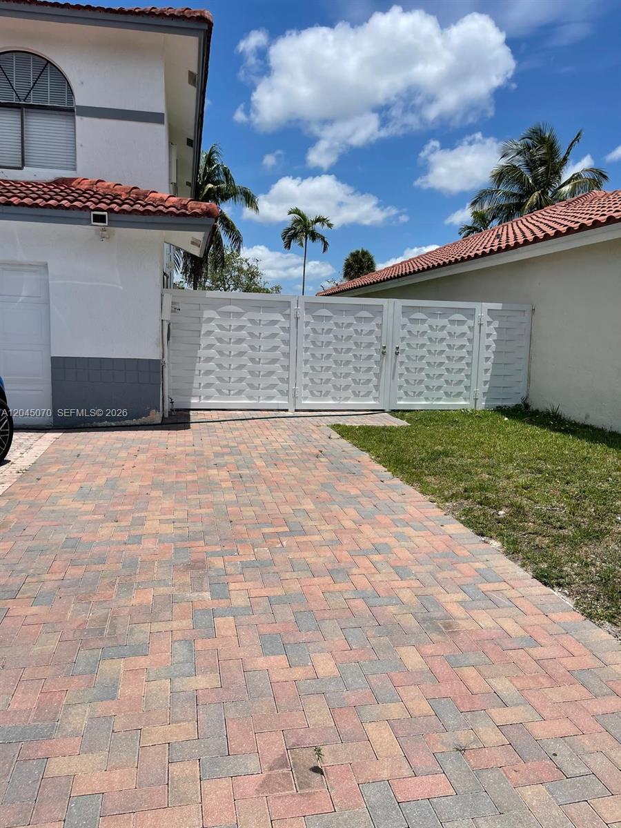 A white gate connects a house to a wall above a brick paver driveway — 15975 SW 109th St # 1, Miami FL 33196, MIAMI, FL