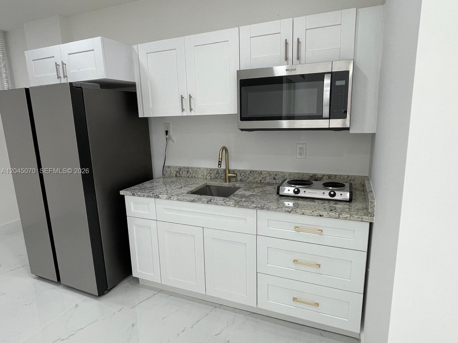 A small kitchen features white cabinets, granite countertops, a stainless steel refrigerator, and a microwave — 15975 SW 109th St # 1, Miami FL 33196, MIAMI, FL