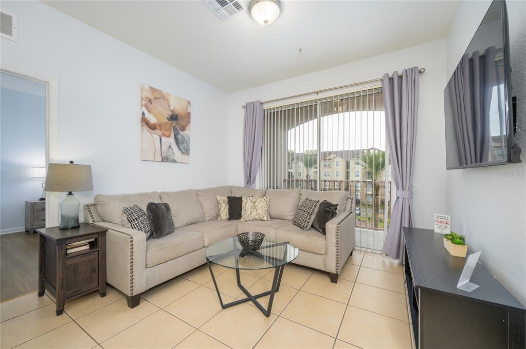 A living room features a beige sectional sofa, glass coffee table, and sliding glass balcony doors — 4862 CAYVIEW AVENUE UNIT 30809, ORLANDO, FL