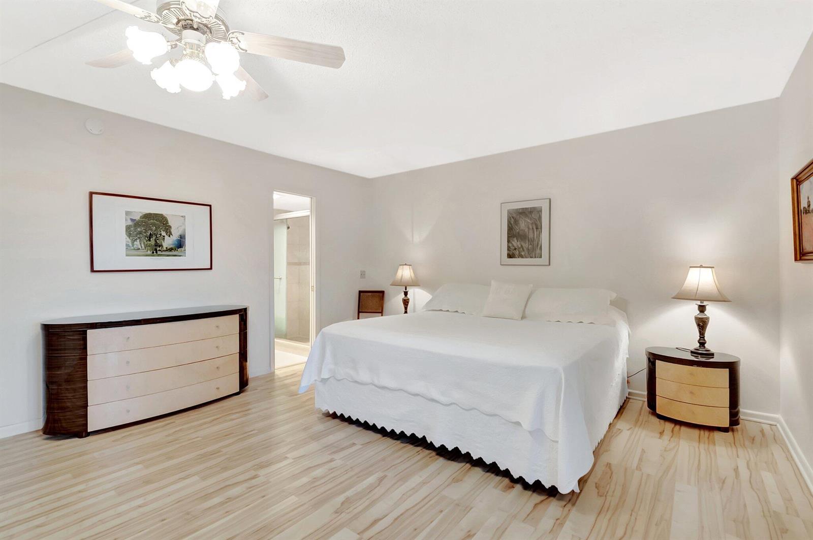 A bedroom with light wood flooring, a white bed, a ceiling fan, and two lamps — 2043 Cambridge C, Deerfield Beach FL 33442, DEERFIELD BEACH, FL