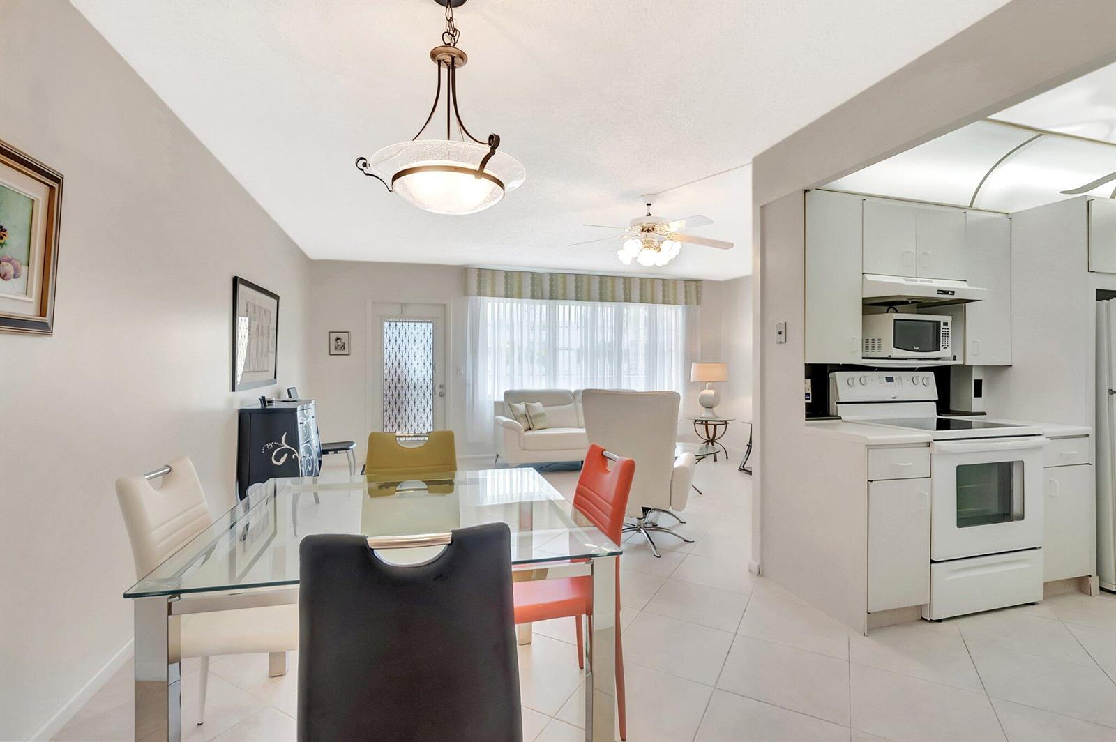 A dining area with a glass table and colorful chairs sits adjacent to a white kitchen — 2043 Cambridge C, Deerfield Beach FL 33442, DEERFIELD BEACH, FL