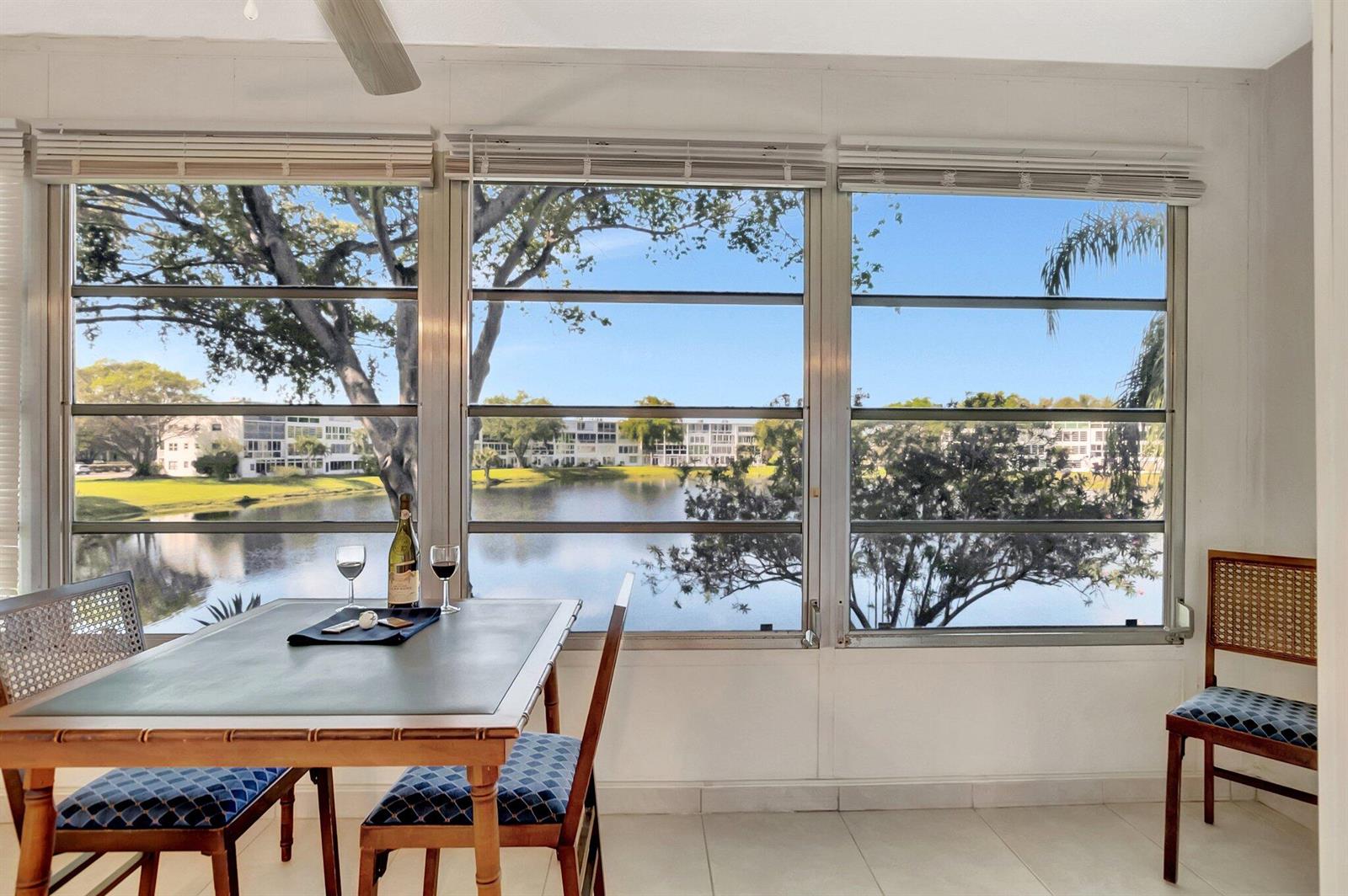 A sunroom with a dining table and chairs overlooks a lake and apartment buildings — 2043 Cambridge C, Deerfield Beach FL 33442, DEERFIELD BEACH, FL