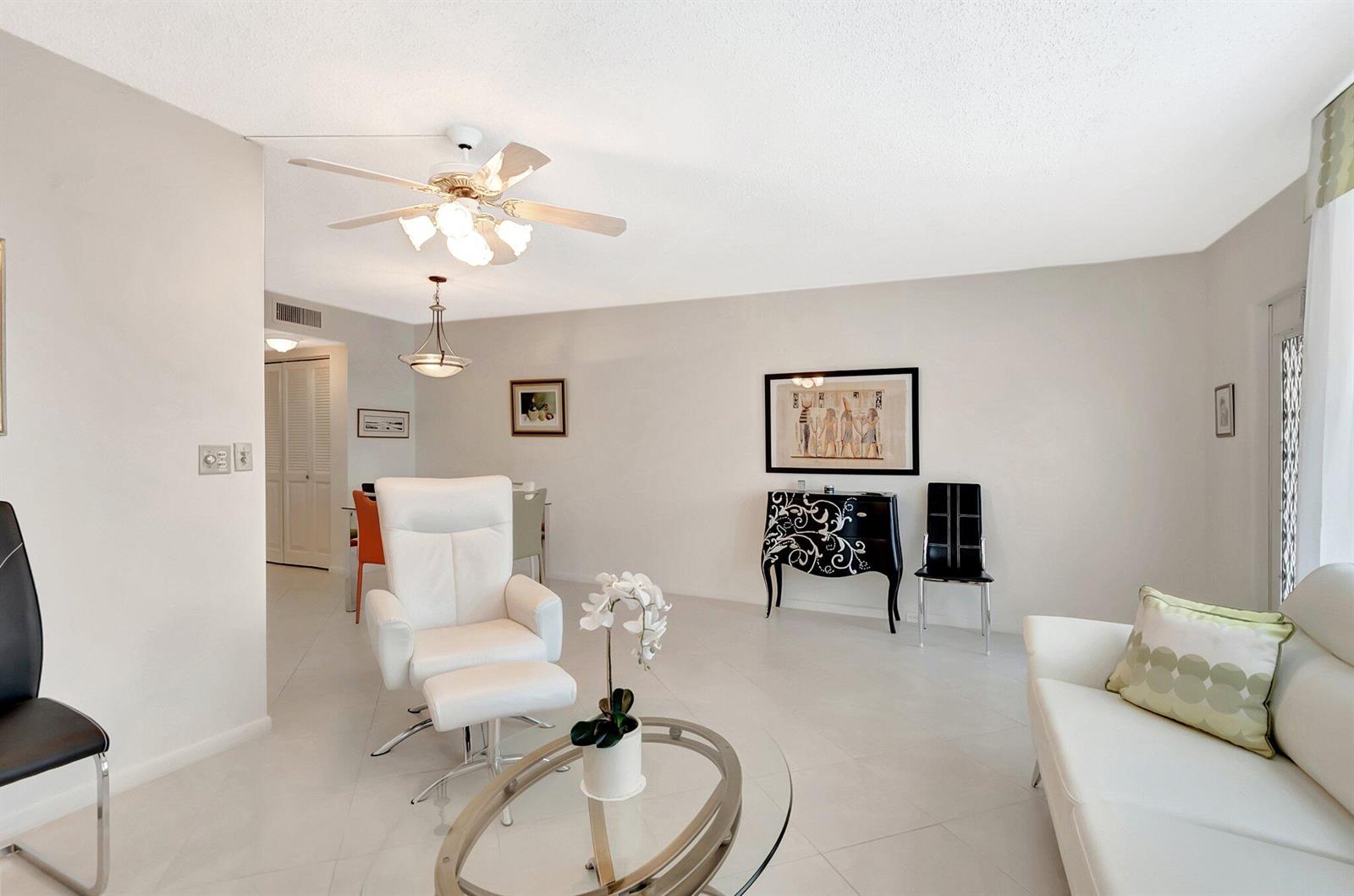 A bright living room features white tile floors, a white leather chair, and modern furniture — 2043 Cambridge C, Deerfield Beach FL 33442, DEERFIELD BEACH, FL