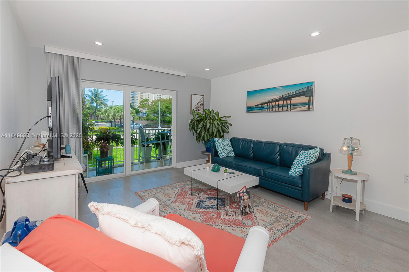 A living room features a blue leather sofa, a patterned rug, and a sliding glass door — 1631 NE 114th St # 112, Miami FL 33181, MIAMI, FL