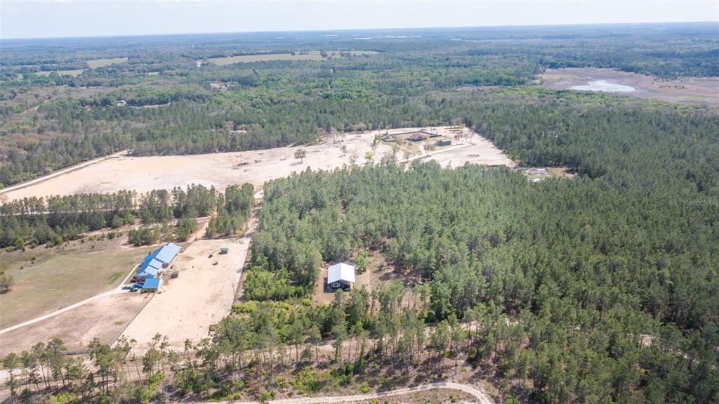 An aerial view shows a rural property with a house, outbuildings, and surrounding forest — 5276 ORGANIC. (POLE BARN) ROAD, MELROSE, FL