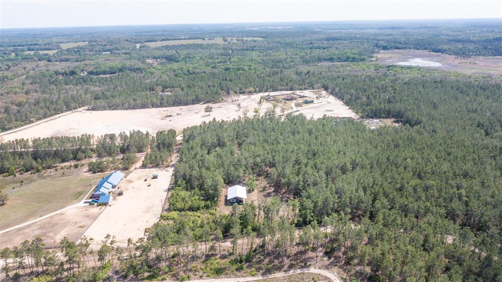 An aerial view shows a rural property with a house, outbuildings, and surrounding forest — 5276 ORGANIC. (POLE BARN) ROAD, MELROSE, FL