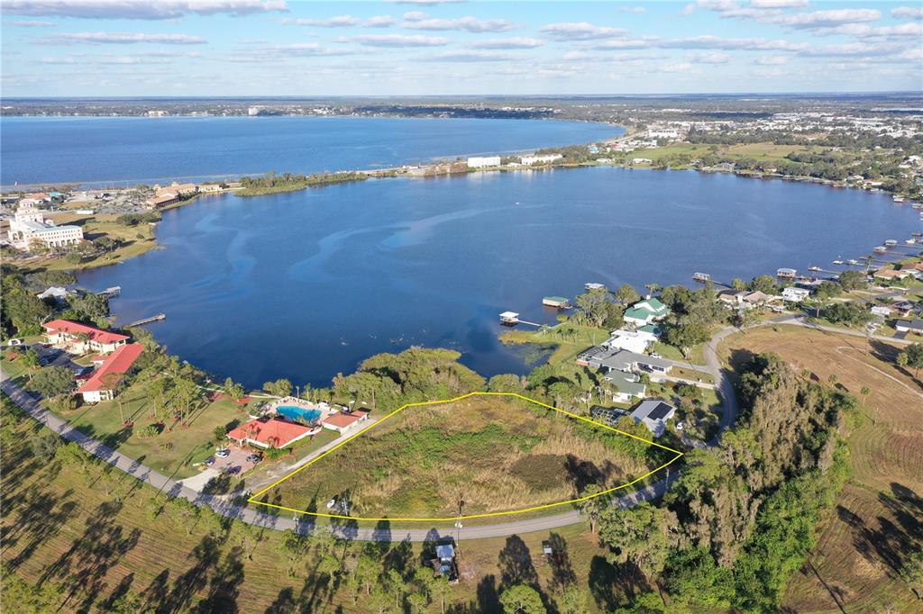 An aerial view shows a vacant, yellow-outlined lot situated next to a lake and houses — 136+142 LAKE DRIVE BOULEVARD, SEBRING, FL