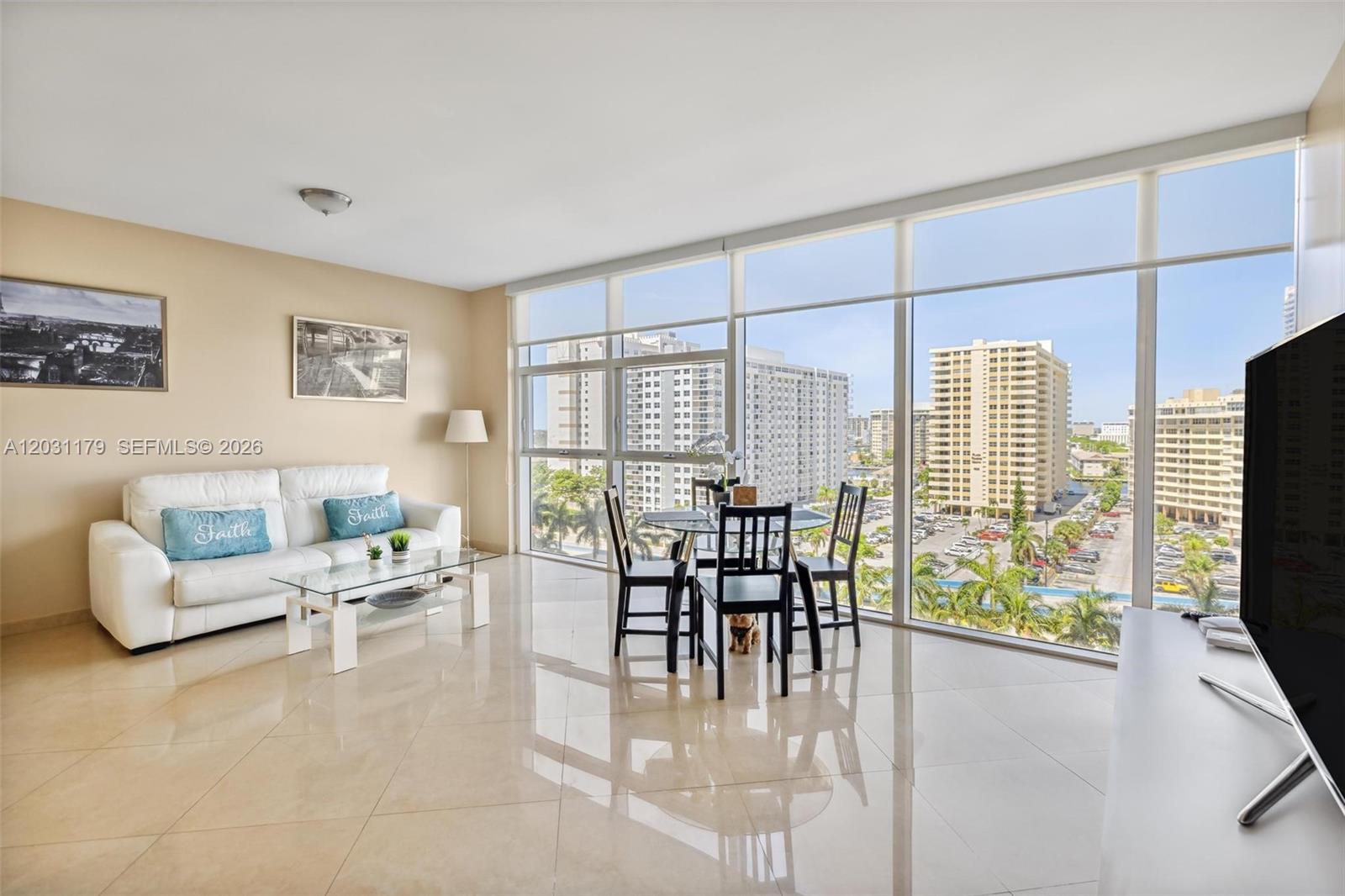 A living room with a white sofa, glass coffee table, dining set, and floor-to-ceiling windows — 1830 S Ocean Dr # 907, Hallandale Beach FL 33009, HALLANDALE BEACH, FL