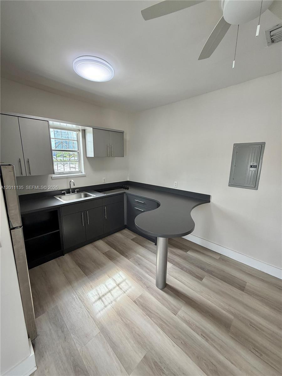 A kitchen features dark gray cabinets, black countertops, a breakfast bar, and light wood flooring — 173 NW 36th St # 2, Miami FL 33127, MIAMI, FL
