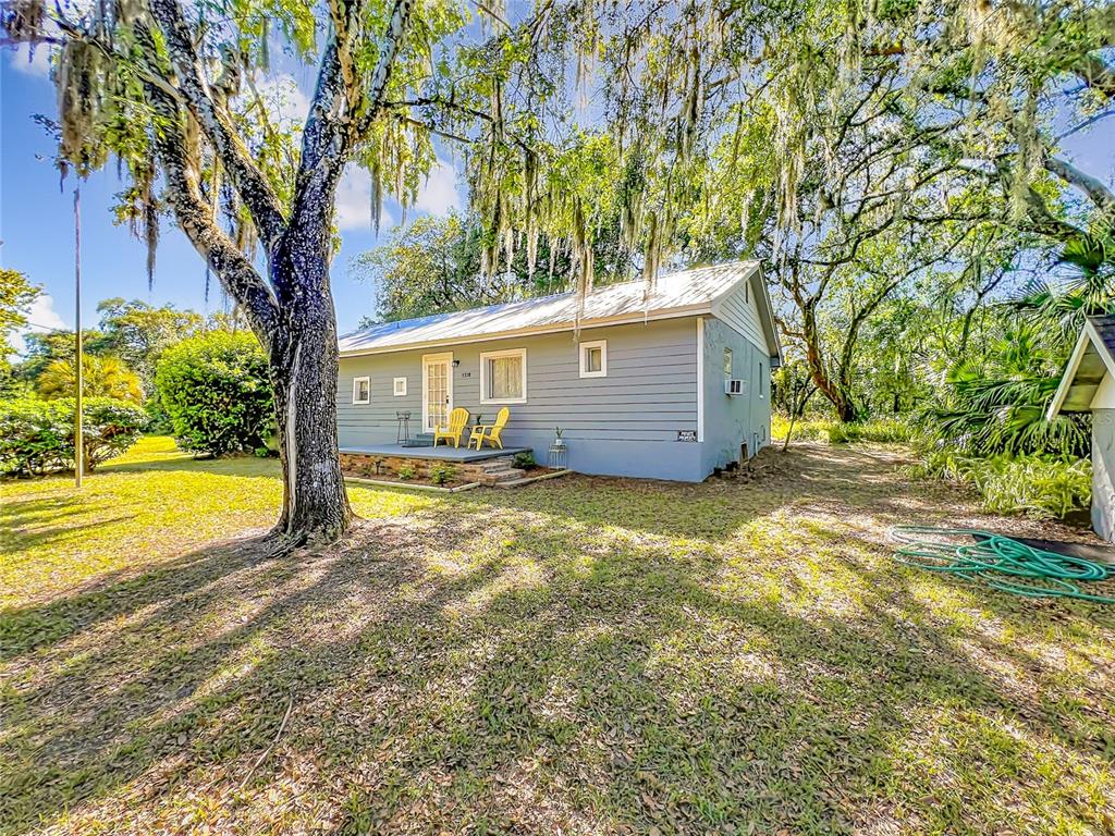 A gray, single-story house with a metal roof sits on a grassy, tree-shaded lot — 1338 SAINT NICHOLAS AVENUE, CHRISTMAS, FL
