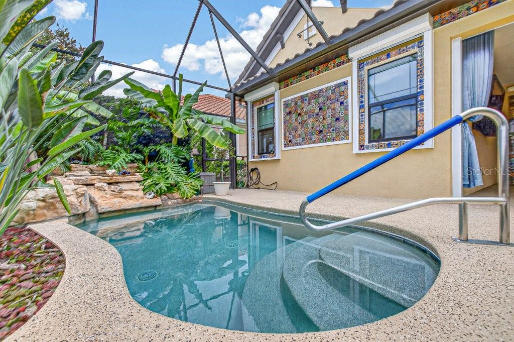 A small backyard pool with a rock waterfall feature sits under a screened-in patio enclosure — 169 ASPEN WAY, PALM COAST, FL