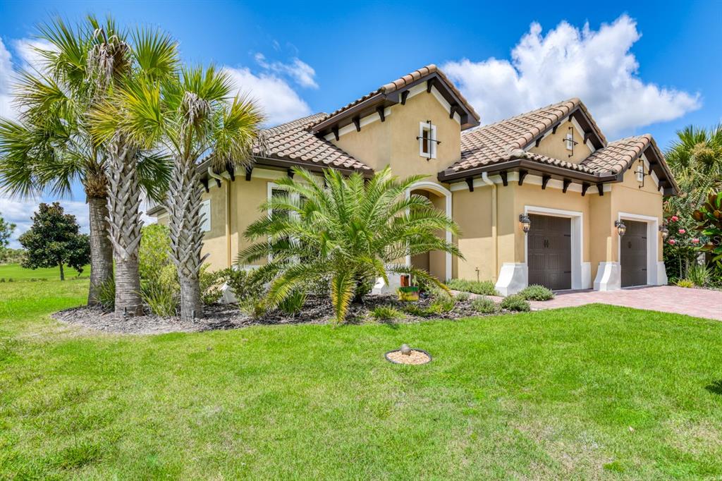 A tan stucco house with a tiled roof, two garage doors, and palm trees outside — 169 ASPEN WAY, PALM COAST, FL