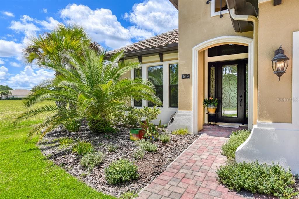 A brick walkway leads to the front entrance of a house with a palm tree — 169 ASPEN WAY, PALM COAST, FL