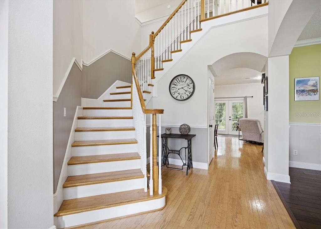 A foyer features a wooden staircase with white railings, hardwood floors, and a wall clock — 519 TEAGARDEN COURT, WINTER GARDEN, FL