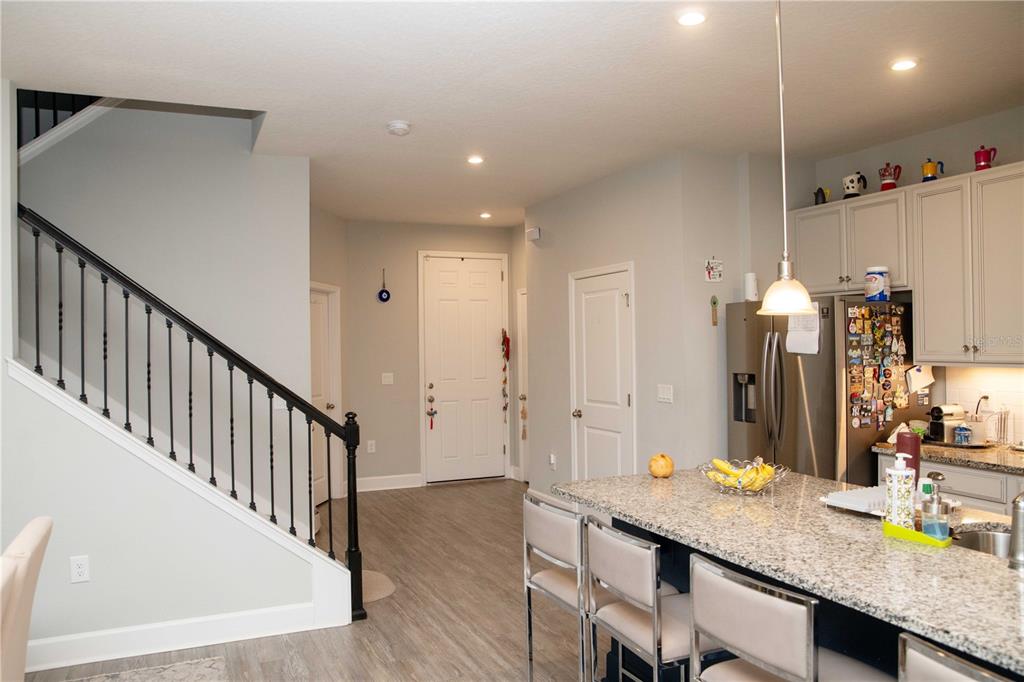 A kitchen with a granite island and stools overlooks a staircase and entryway — 5963 GLORY BOWER DRIVE, WINTER GARDEN, FL