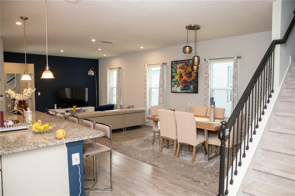 An open-concept living and dining area features a kitchen island, staircase, and dark accent wall — 5963 GLORY BOWER DRIVE, WINTER GARDEN, FL