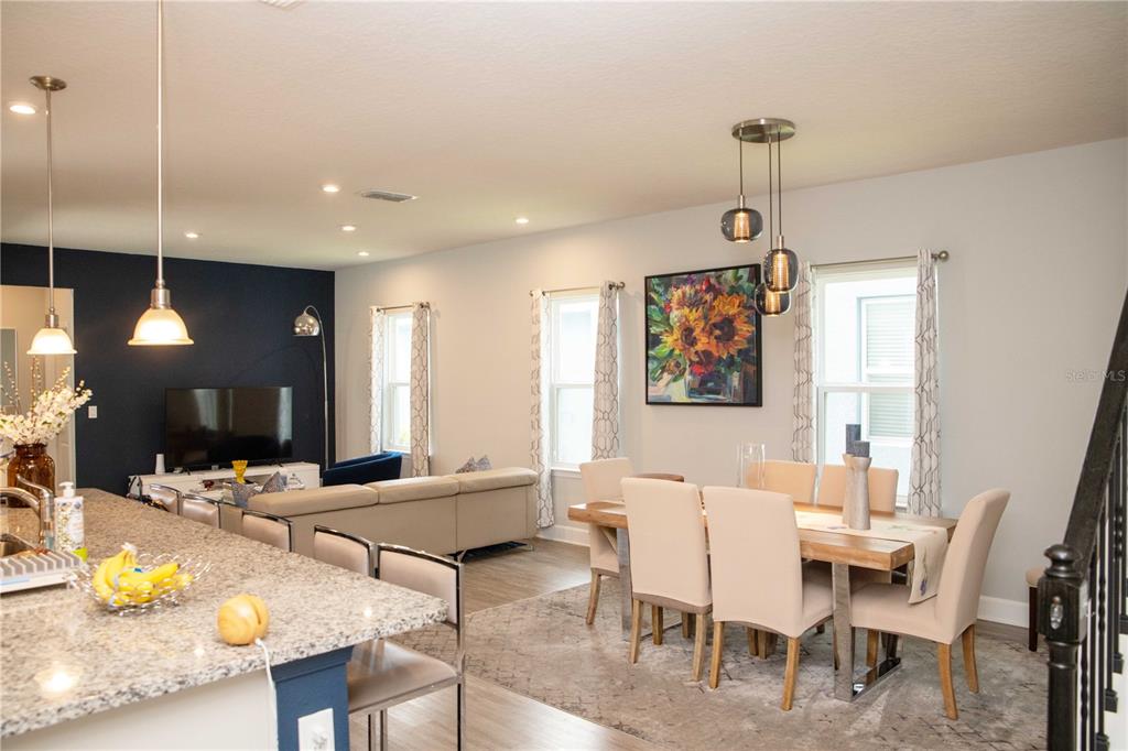 An open-concept living and dining area features a kitchen island, neutral furniture, and modern lighting — 5963 GLORY BOWER DRIVE, WINTER GARDEN, FL