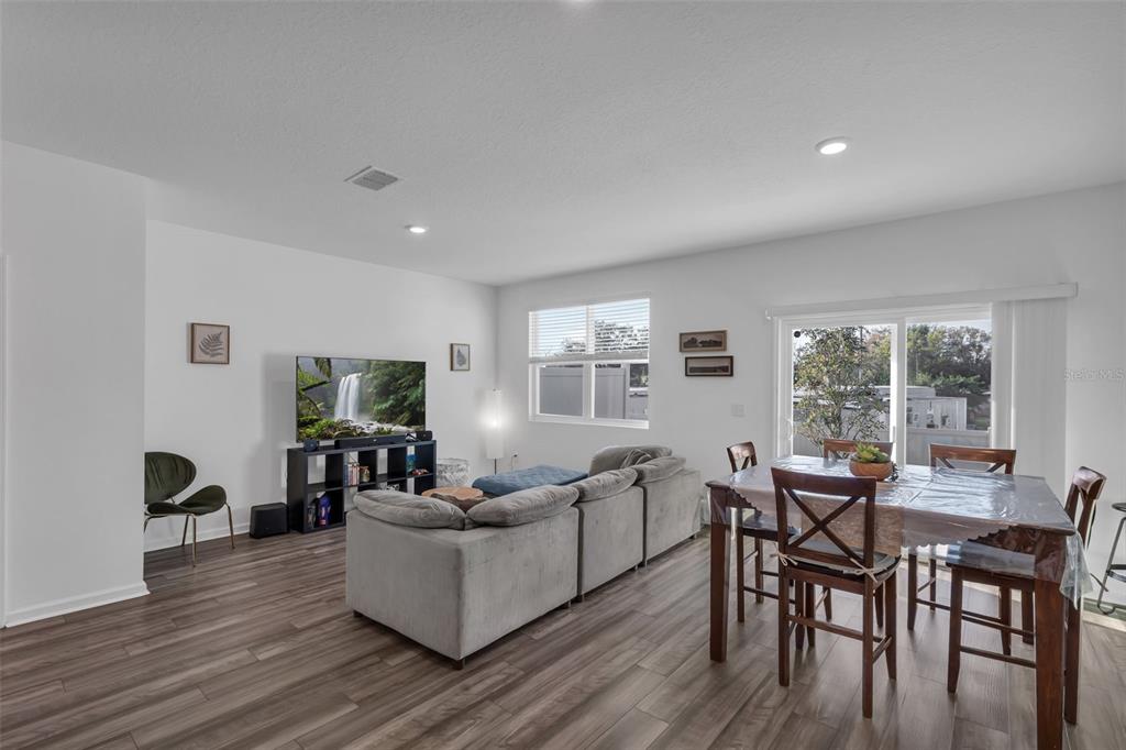 A living and dining area with wood-look flooring, a gray sectional sofa, and a television — 6359 KAY MORGAN LANE, GIBSONTON, FL