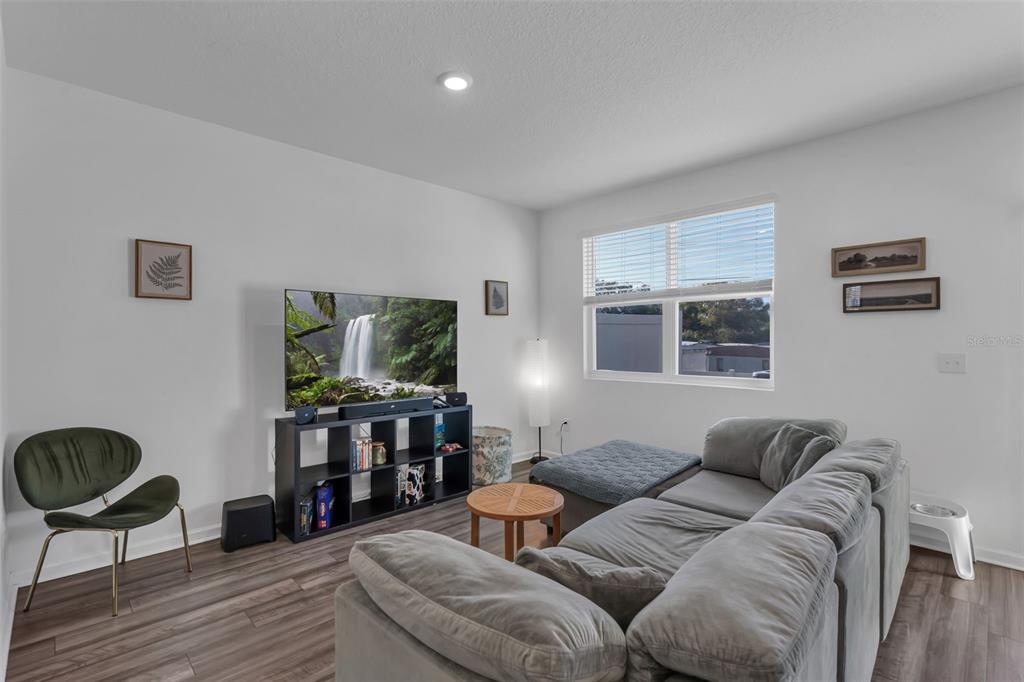 A living room features a grey sectional sofa, a television on a black shelf, and wood-look flooring — 6359 KAY MORGAN LANE, GIBSONTON, FL